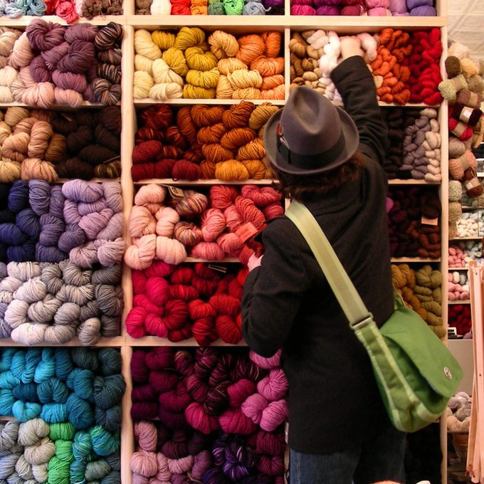Shelves of colorful yarn skeins in a yarn shop, with a shopper reaching for a skein