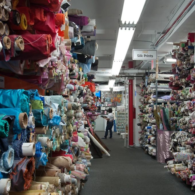 Aisles of colorful rolled fabric bolts stacked floor to ceiling in a fabric store